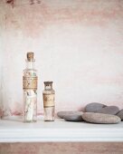 Two corked glass bottles with vintage labels and flat pebbles in front of patinated wall