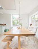 Dining table, bench and white chairs in open-plan light-flooded kitchen-dining room