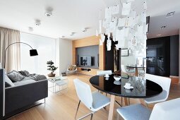 Esstisch mit schwarzer, runder Platte und weiße Stühle unter Designer-Pendelleuchte Zettel'z in offenem Wohnraum mit Loungebereich