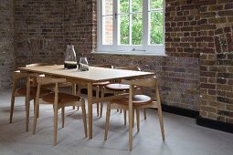 Dining area with classic chairs around wooden table in loft interior with rustic brick wall
