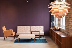 Armchair with beige upholstery, pale sofa and ottoman against purple wall; PH Artichoke Pendant lamp in foreground