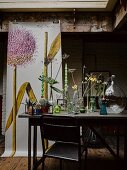 Verschiedene Vasen mit Blumen auf Tisch, im Hintergrund Poster mit Zwiebelblüte-Motiv
