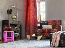Wohnbereich in afrikanischem Stil - Sideboard, roter Vorhang, Sofa mit gemustertem Bezug und Lederpouf