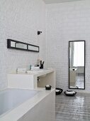 Fitted bathtub, masonry washstand and full-length mirror against whitewashed brick walls