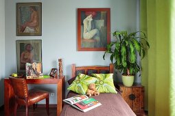 Bett zwischen Arbeitsplatz und Beistelltisch mit Grünpflanze, an Wand Bildersammlung mit Frauenmotiv