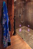 Shower areas with glass partition, brown mosaic tiles on walls and floor and dressing gown hanging to one side in designer bathroom