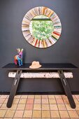 Round mirror with colourful frame and dark wooden table against black wall