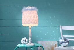 Lampshade hand-made from plastic spoons and feather trim in front of turquoise background