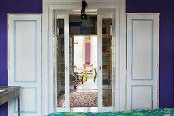 Blick von Raum mit lila Wand und Doppeltür mit hellblauem Kassettenrahmen auf buntes Kinderzimmer im Hintergrund