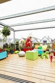 Spielendes Kind auf grosser, verglaster Dachterrasse mit Holzbelag und Pflanztöpfen zwischen farbenfroher Ausstattung
