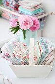 Folded, rose-patterned fabrics in pastel shades arranged in white wooden trug - vintage ambiance
