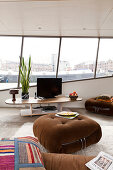 Brown ottoman in front of flatscreen TV on low table with view of harbour though strip of windows in background