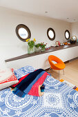 Bed, retro armchair, fitted sideboard and portholes in houseboat bedroom