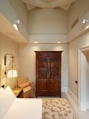Antique, carved cupboard in high-ceilinged, elegant bedroom