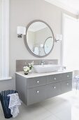 Washstand with grey drawers and large round mirror in elegant bathroom