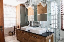 Bathroom in modern, traditional style with solid-wood washstand and two chandeliers in front of glazed shower area