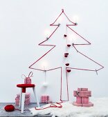 Silhouette of Christmas tree made from red wool on wall above stool wrapped in yarn