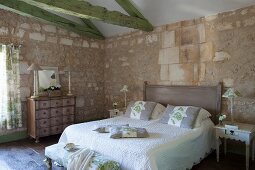 Mediterranes Schlafzimmer mit Natursteinwänden und grün gestrichenen Deckenbalken, antike Kommode und gequiltete Tagesdecke