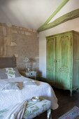 Mediterranes Schlafzimmer mit Natursteinwänden und grün gestrichenen Deckenbalken, die zum grünen antiken Schrank passen