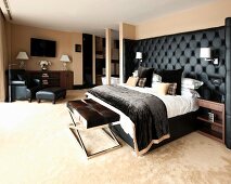 Bed with black upholstered headboard, bench and reading chair in masculine bedroom