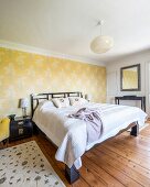 Ländliches Schlafzimmer mit Doppelbett vor tapezierter Wand mit floralem Muster auf gelbem Grund