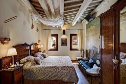 Traditionelles Schlafzimmer mit rustikaler Holzbalkendecke, antiken Möbeln, seitlich Nachttisch mit Tischleuchte neben Doppelbett