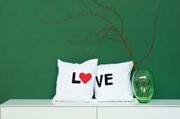 Hand-sewn scatter cushions with lettering reading 'LOVE' next to green glass vase