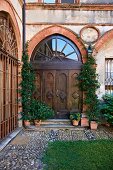 Carved double door in ogee arch and and climbing plants in terracotta pots on front steps