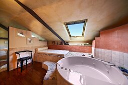 Modern, oval bathtub with massage jets in modern bathroom with sloping ceiling in Italian shades of terracotta