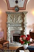 Vase of roses on table in front of open fireplace with carved stone surround (Hotel Villa Cimbrone)