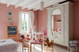 Nostalgisches Kinderzimmer mit rosafarbenen Wänden, einem Spieltisch und antikem Schrank