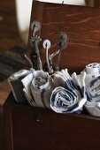 Gerollte Küchenhandtücher und Vintage Perforierwerkzeuge in alter Holzkiste mit offenem Deckel