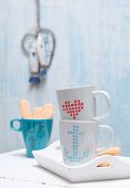 Plain coffee mugs decorated with cross-stitch patterns drawn on with porcelain pen