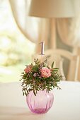Kugelförmige Glasvase mit Rosengesteck und eingesteckter Tischnummer