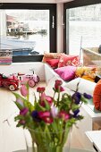 Colourful scatter cushions on couch against large windows of houseboat with view of water