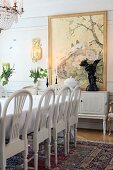 White-painted chairs with arched backrests around dining table in traditional dining room with painting on wall in background