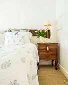 Antiker Nachttisch mit Rosenstrauss und Lampe neben Bett