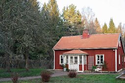 View of Falu-red wooden house with white windows seen from garden