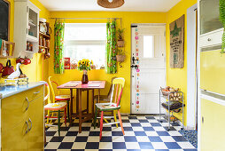 Colourful chairs in yellow kitchen-dining room with chequered floor