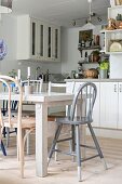 Verschiedene Stühle um weiss lasierten Esstisch in Einbauküche, weiss lackierte Küchenschränke im Landhausstil