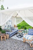 Lounge area in furnished garden pavilion with airy fabric curtains on gravel terrace