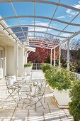 French bistro furniture and planters on sunny terrace below curved metal pergola below blue sky