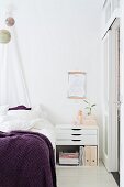 Modern bedside cabinet with drawers and purple blanket on bed below suspended globes