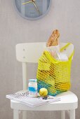 A homemade, yellow crocheted shopping bag on a white kitchen chair