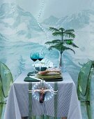 Dining table with green plexiglas chairs in front of wall with mountain landscape & fairy lights