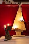 Wooden Christmas tree decorated with tealights and angel figurine holding candle in front of red wainscoting