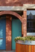 Reihenhauseingang mit türkisfarbenen Eingangstüren, holzverkleidetem Pflanzbehälter und Sandstein-Rundbogen im Belle Epoque Stil