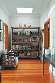 Armchair with rattan frame on wooden floor in front of rustic, modern shelving in hallway with skylight