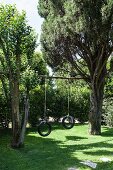 Two tyre swings hanging from pole between trees in summery garden