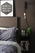 Pendant lamp with bulb above bedside table next to bed against dark, painted wall